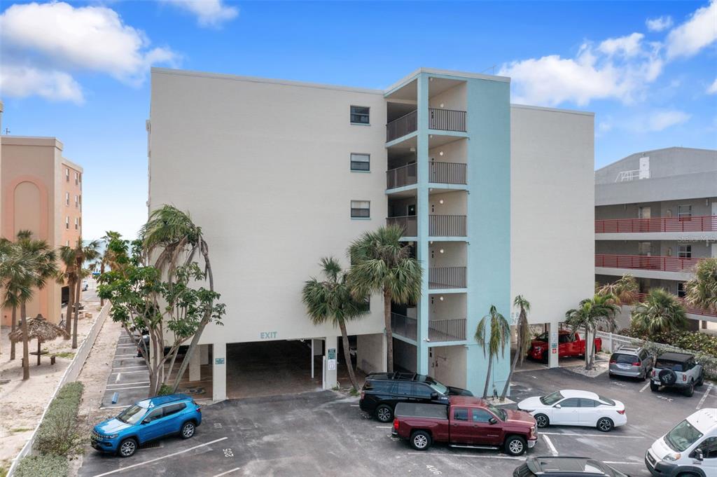 An exterior view of a multi-story apartment building with a parking garage and palm trees — 12924 GULF BOULEVARD UNIT 502, MADEIRA BEACH, FL