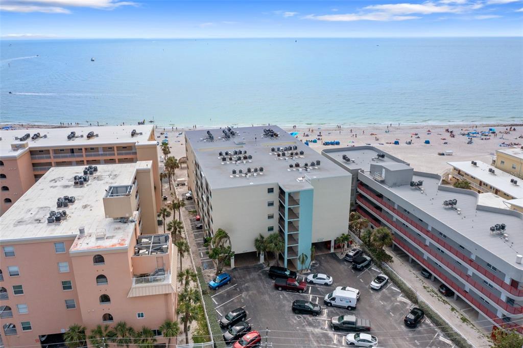 An aerial view shows a multi-story apartment building with a parking lot near the beach — 12924 GULF BOULEVARD UNIT 502, MADEIRA BEACH, FL