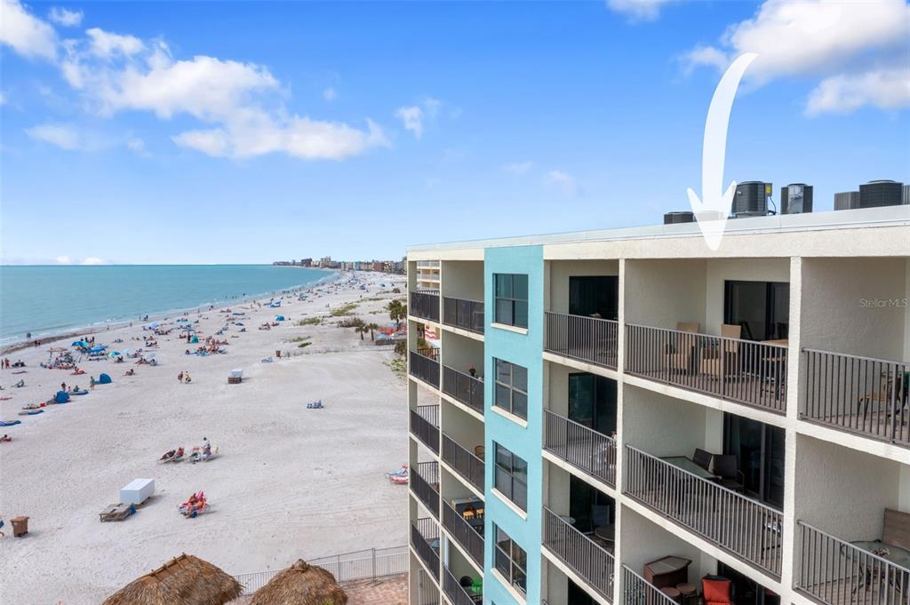 An exterior view of a multi-story beachfront building showing balconies overlooking a sandy beach — 12924 GULF BOULEVARD UNIT 502, MADEIRA BEACH, FL