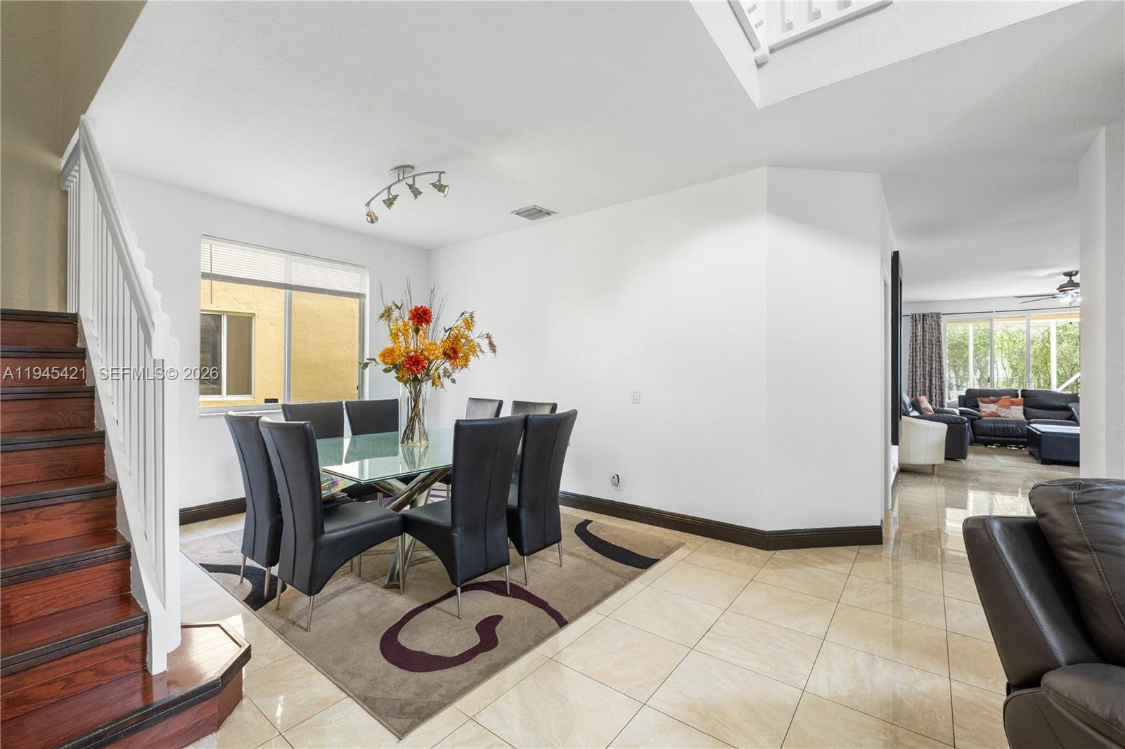 A dining area features a glass table, black chairs, and a staircase with wooden steps — 1199 Golden Cane Dr, Weston FL 33327, WESTON, FL
