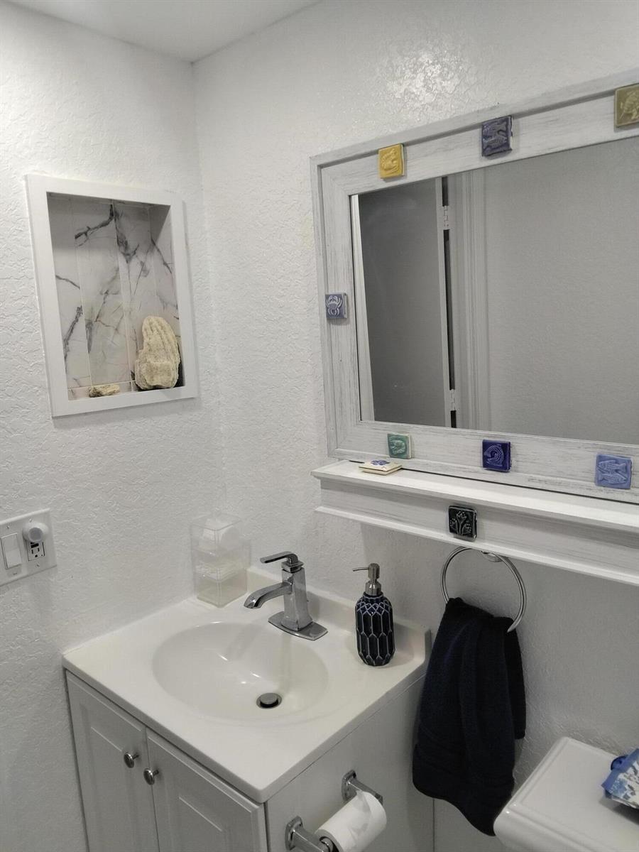 A bathroom vanity with a white cabinet, marble-look wall niche, and a decorative framed mirror — 399 Brittany Drive # I, Delray Beach FL 33446, DELRAY BEACH, FL