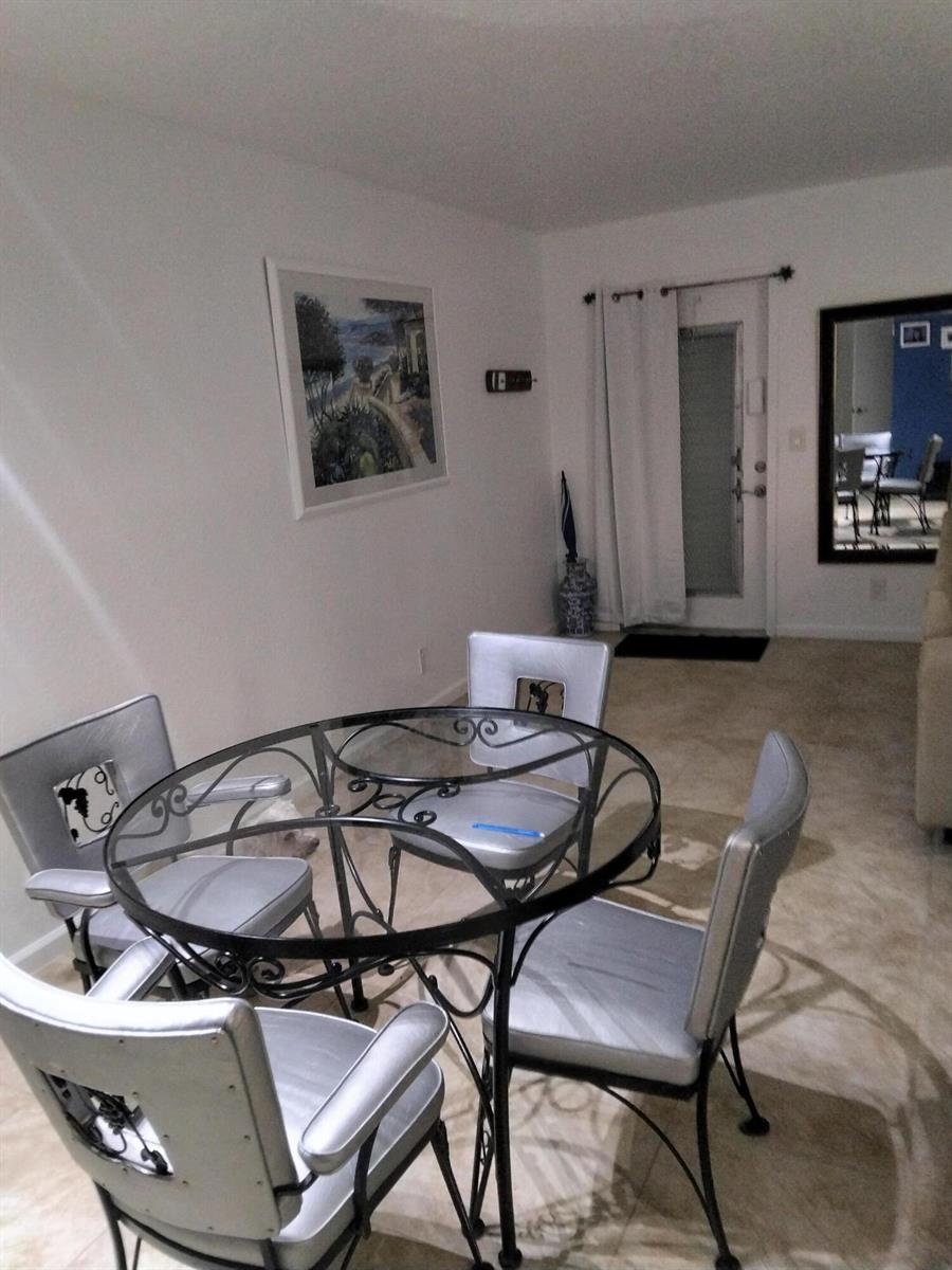 A dining area features a round glass table with four silver chairs on tile flooring — 399 Brittany Drive # I, Delray Beach FL 33446, DELRAY BEACH, FL