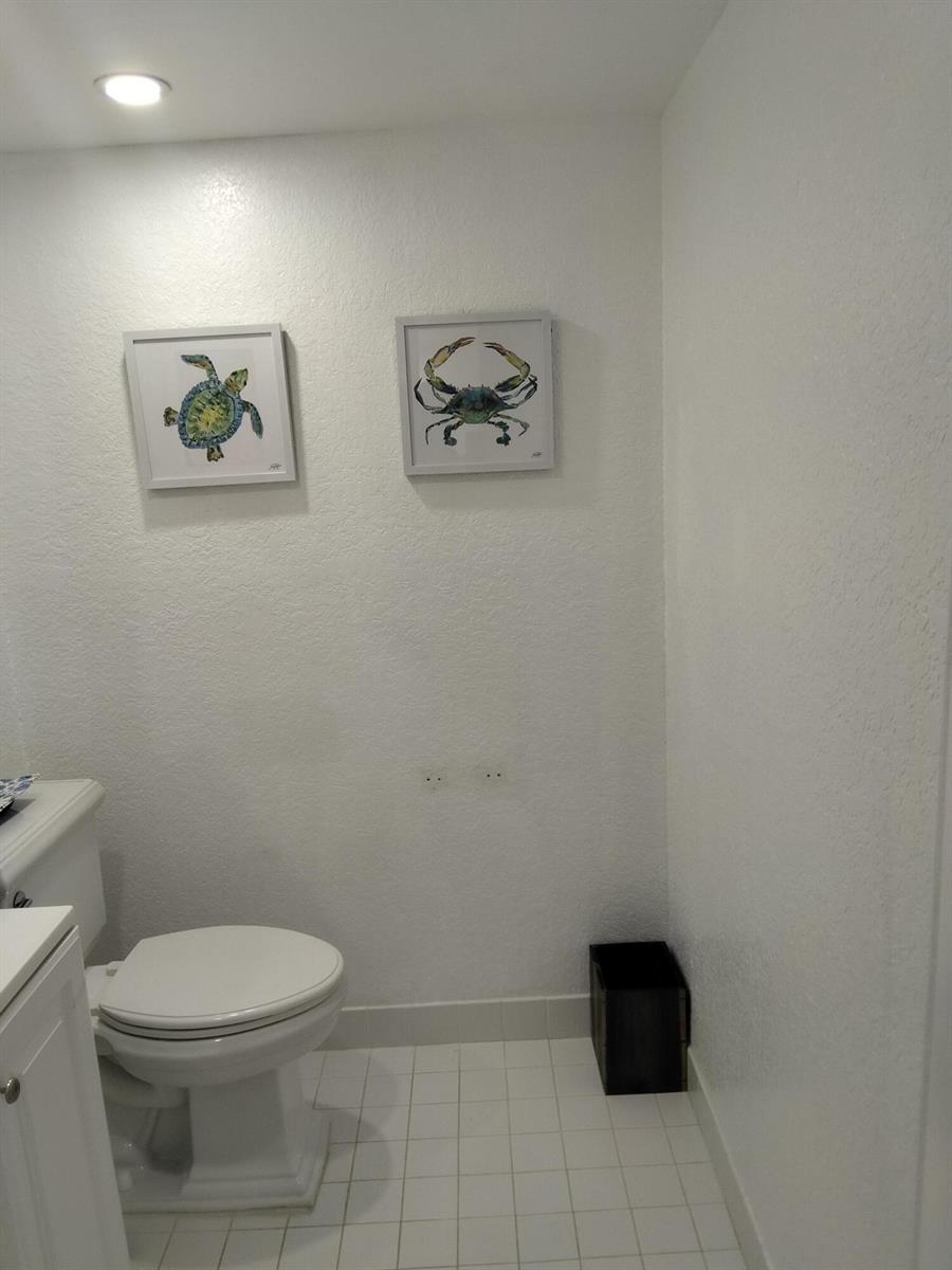 A bathroom features a white toilet, tiled floor, and two framed sea creature wall prints — 399 Brittany Drive # I, Delray Beach FL 33446, DELRAY BEACH, FL