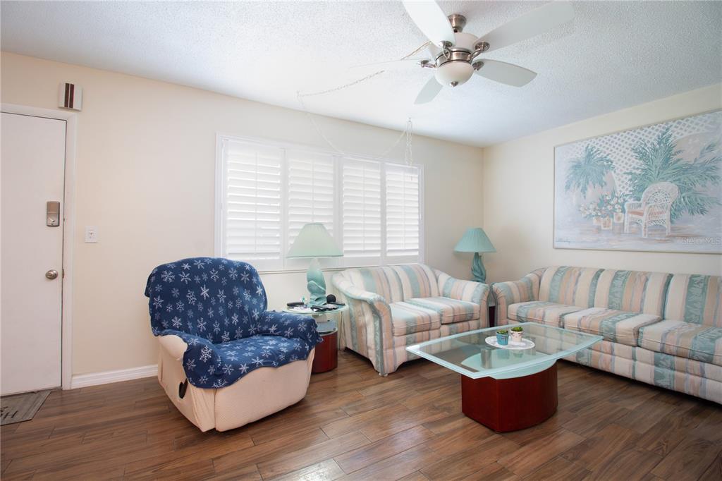 A living room with wood-look tile flooring, a ceiling fan, and striped upholstered furniture — 5267 81ST STREET N UNIT 21, ST PETERSBURG, FL