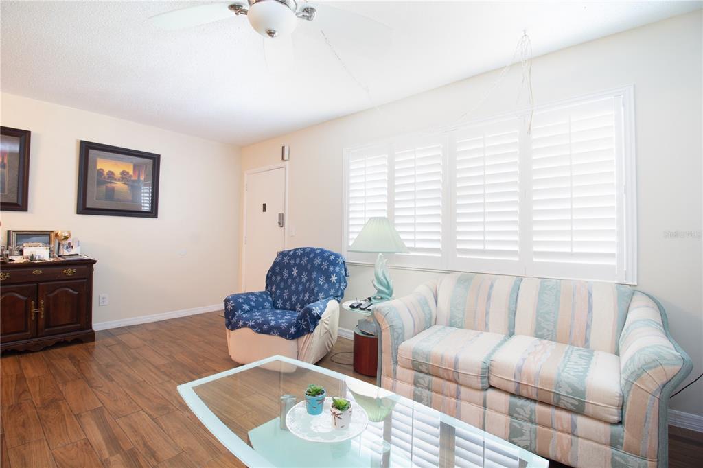 A living room features a striped sofa, a blue patterned armchair, and wood-look flooring — 5267 81ST STREET N UNIT 21, ST PETERSBURG, FL