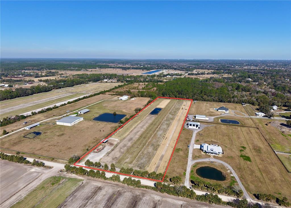 An aerial view shows a rectangular plot of land featuring a long dirt airstrip — 3761 STRAWBERRY LANE, NEW SMYRNA BEACH, FL