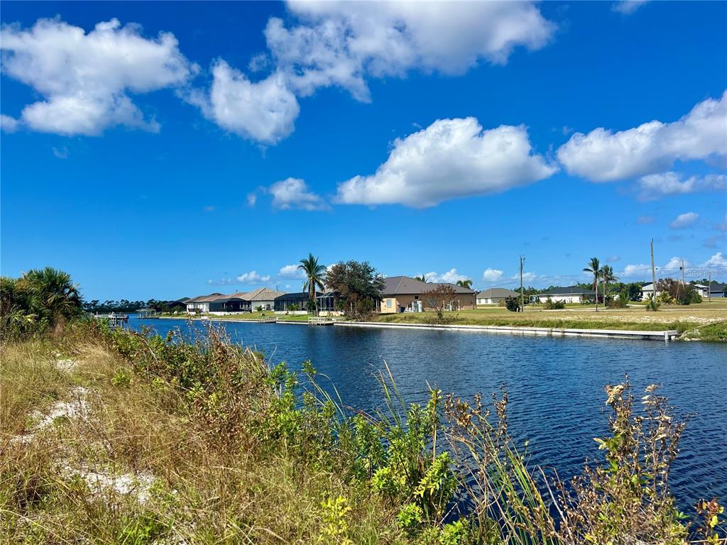 A canal view showing residential houses along the waterfront under a blue sky with clouds — 4103 NW 39TH STREET, CAPE CORAL, FL