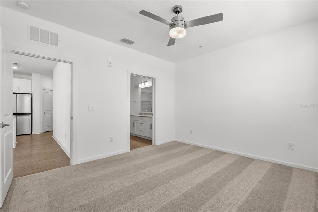 A bedroom with beige carpet, white walls, a ceiling fan, and doorways leading to other rooms — 1700 RANCH ROAD UNIT B3-6215, NOKOMIS, FL