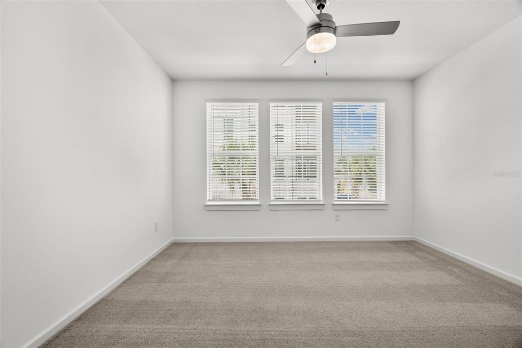 A bright, empty bedroom features white walls, beige carpeting, a ceiling fan, and three windows — 1700 RANCH ROAD UNIT B3-6215, NOKOMIS, FL