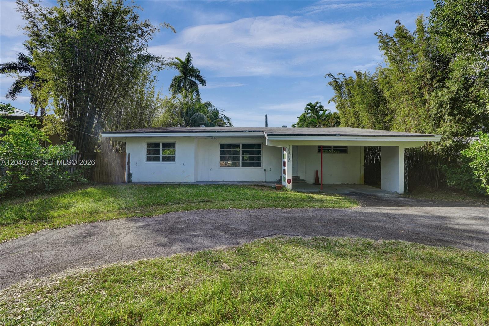 A single-story white house features a flat roof, a carport, and a curved asphalt driveway — 18500 NE 23rd Ct, Miami FL 33180, MIAMI, FL