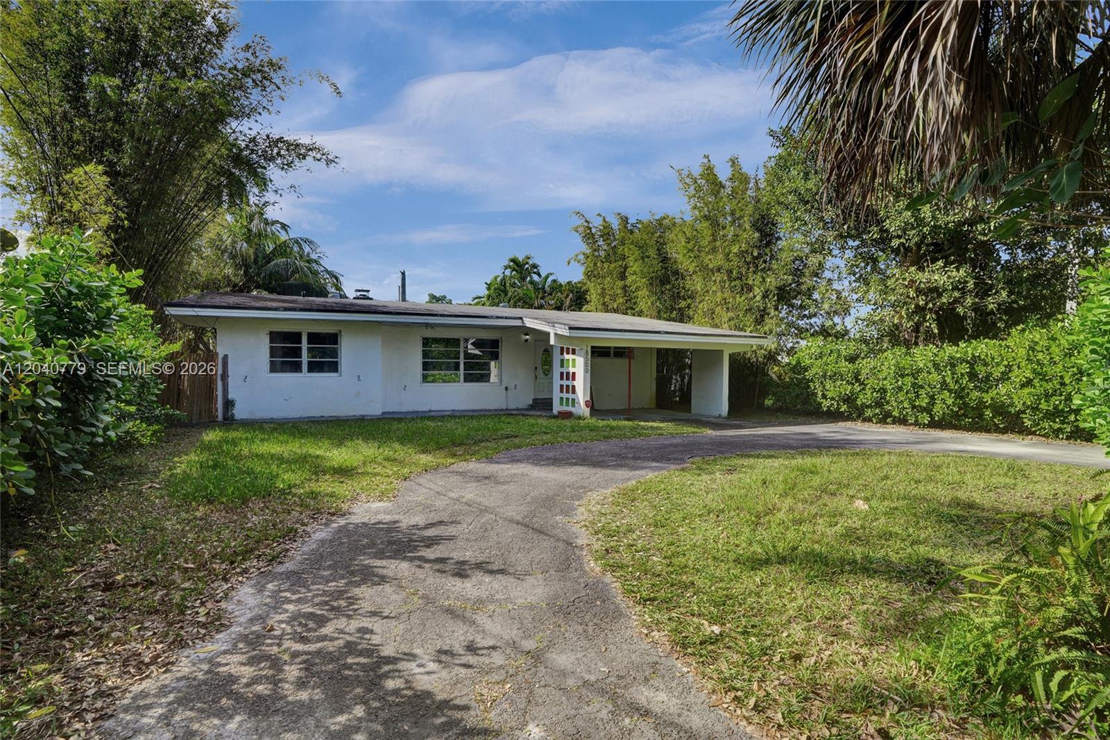 A single-story white house with a carport and a curved driveway sits on a lawn — 18500 NE 23rd Ct, Miami FL 33180, MIAMI, FL