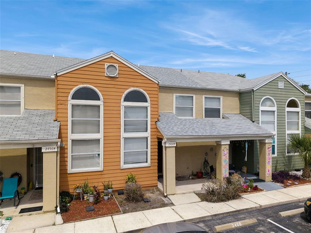 An exterior view of two adjacent townhouses with tan and green siding and arched windows — 2460 SUMMERFIELD WAY, KISSIMMEE, FL