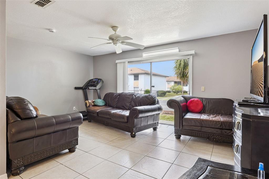 A living room features tile flooring, three dark leather sofas, a treadmill, and sliding doors — 2460 SUMMERFIELD WAY, KISSIMMEE, FL