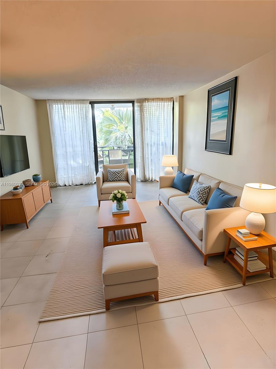 A living room features a beige sofa, armchair, ottoman, coffee table, and a balcony view — 100 Ocean Lane Dr # 303, Key Biscayne FL 33149, KEY BISCAYNE, FL