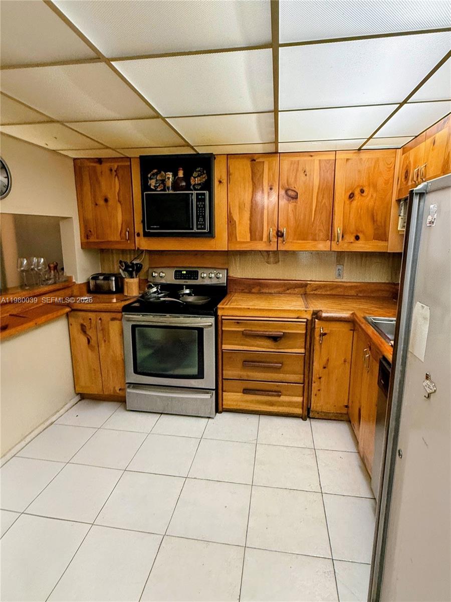 A kitchen features knotty pine cabinets, stainless steel appliances, and a white tiled floor — 100 Ocean Lane Dr # 303, Key Biscayne FL 33149, KEY BISCAYNE, FL