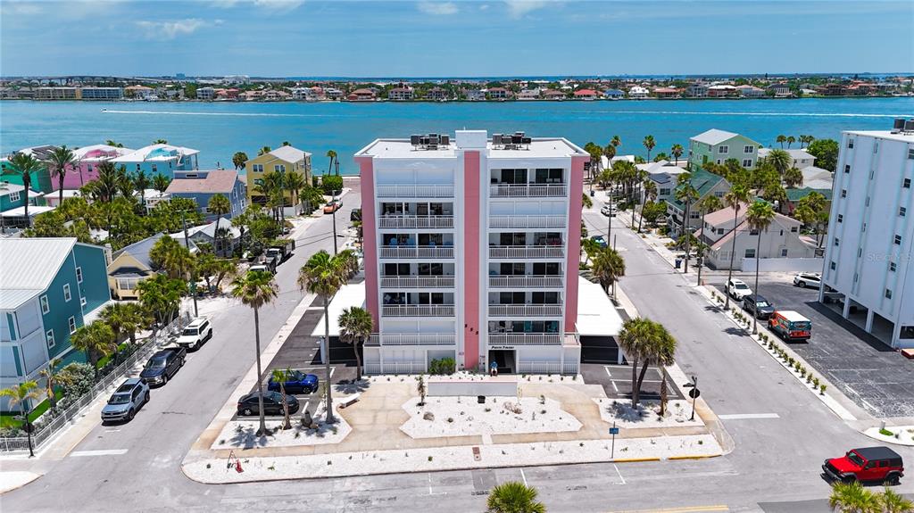 An aerial view shows a multi-story residential building with a pink facade near water — 555 GULF WAY UNIT 6S, ST PETE BEACH, FL