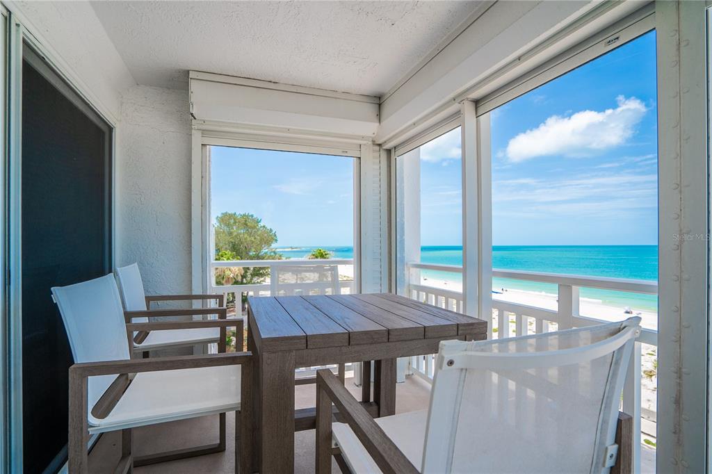 A balcony with a wooden table and chairs overlooks a sandy beach and the ocean — 555 GULF WAY UNIT 6S, ST PETE BEACH, FL
