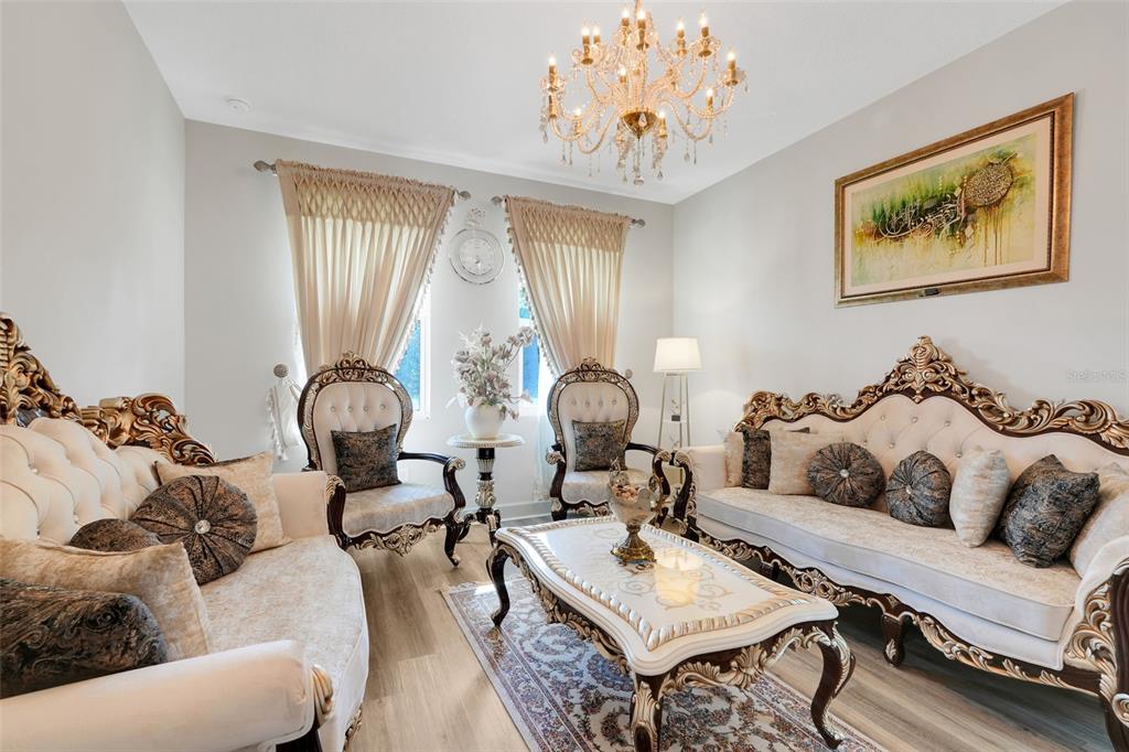 A formal living room features ornate gold-trimmed furniture, a crystal chandelier, and beige curtains — 10169 SPRING LAKE DRIVE, CLERMONT, FL