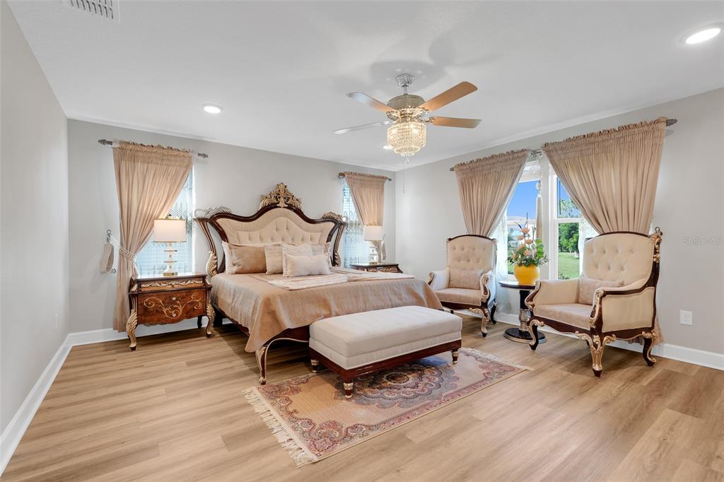 A bedroom features a large ornate bed, two armchairs, a ceiling fan, and light wood flooring — 10169 SPRING LAKE DRIVE, CLERMONT, FL