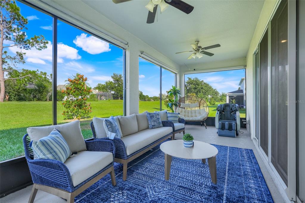 A screened-in patio features wicker furniture, a blue area rug, and views of a grassy yard — 10169 SPRING LAKE DRIVE, CLERMONT, FL