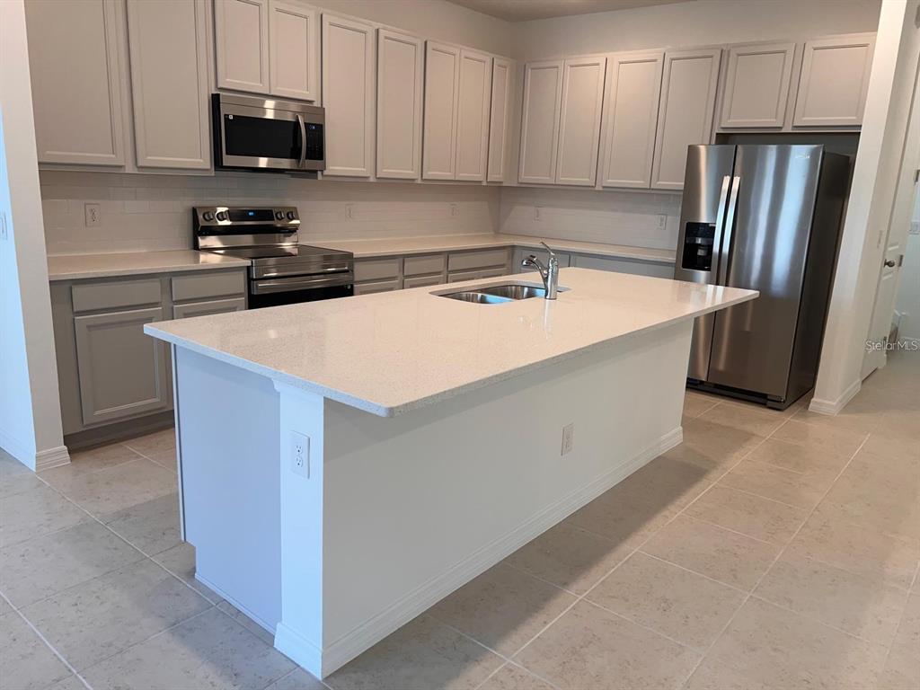 A kitchen features light gray cabinets, white countertops, a central island, and stainless steel appliances — 17820 SHARP PUMMELO ALLEY, WINTER GARDEN, FL