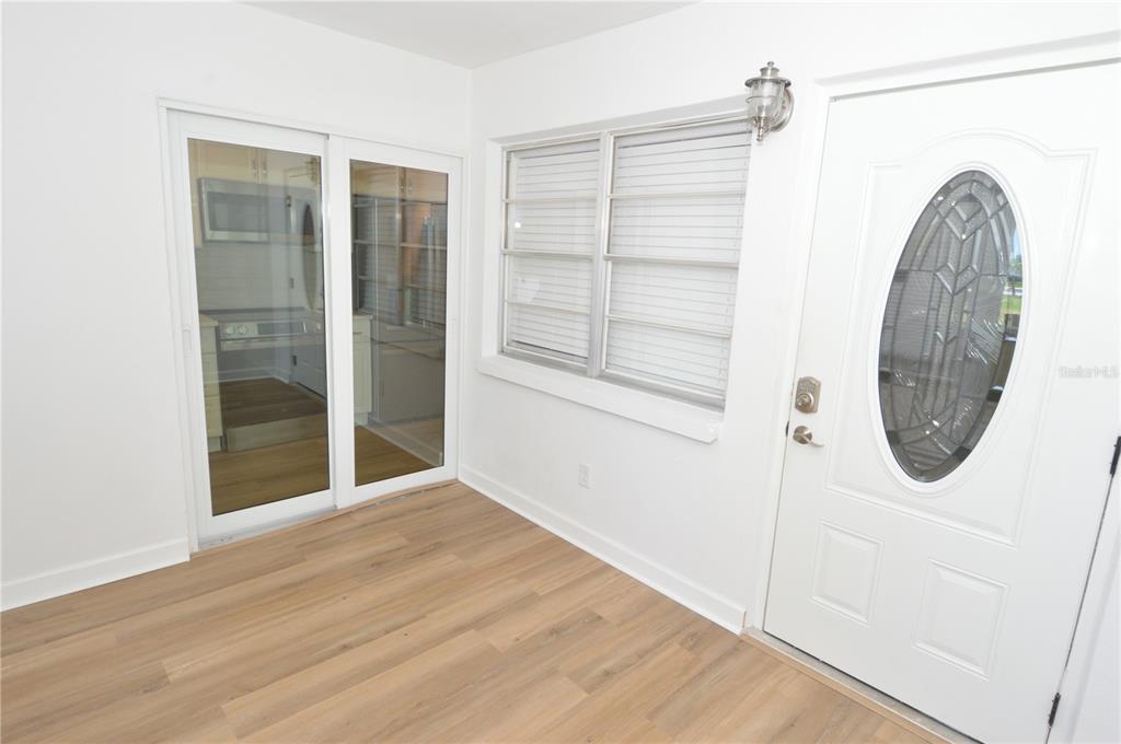 A bright room features light wood-look flooring, a sliding glass door, and a white front door — 4700 COVE CIRCLE UNIT 107, ST PETERSBURG, FL