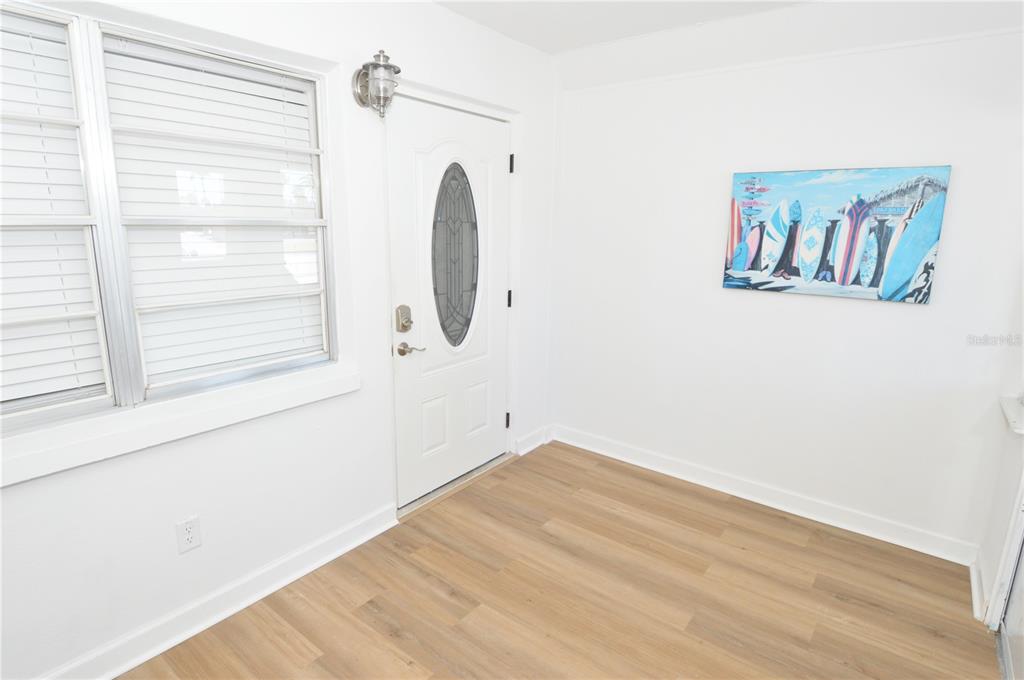 An entryway features light wood-look flooring, white walls, a white front door, and a window — 4700 COVE CIRCLE UNIT 107, ST PETERSBURG, FL