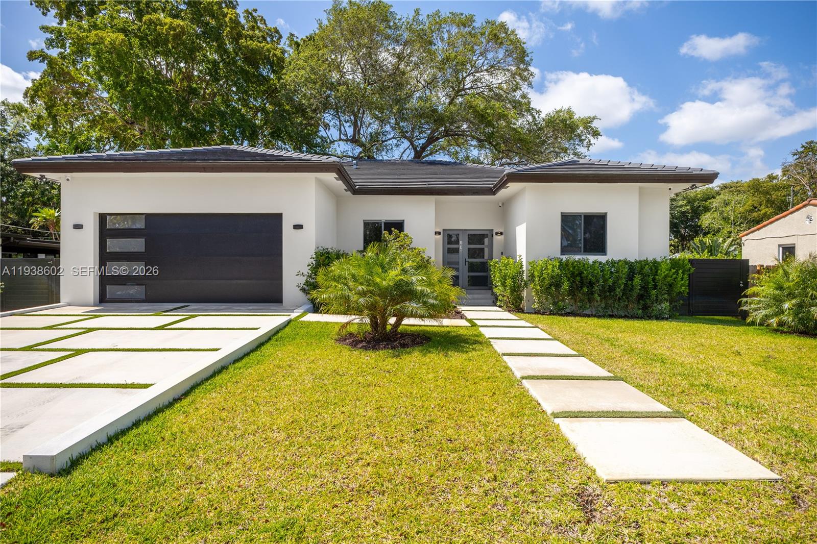 A modern single-story house with a dark garage door and a concrete paver walkway — 1030 NE 121st St, Biscayne Park FL 33161, BISCAYNE PARK, FL