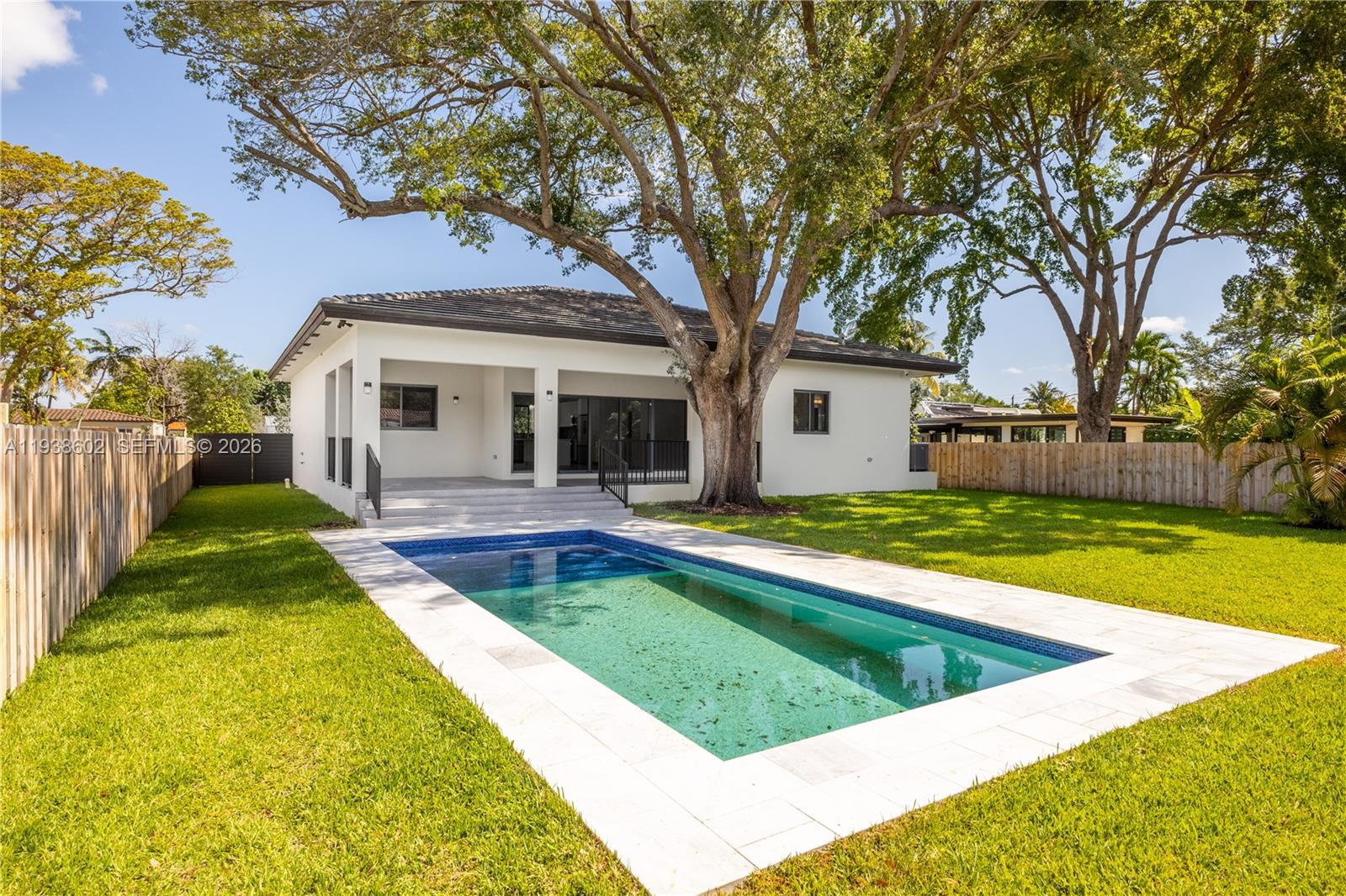 A white house with a rectangular swimming pool and large trees in the backyard — 1030 NE 121st St, Biscayne Park FL 33161, BISCAYNE PARK, FL