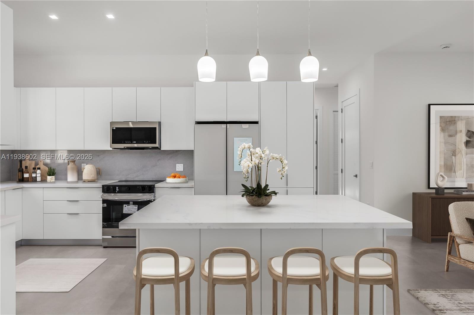 A modern kitchen features white cabinetry, a large marble island, and four wooden bar stools — 1030 NE 121st St, Biscayne Park FL 33161, BISCAYNE PARK, FL