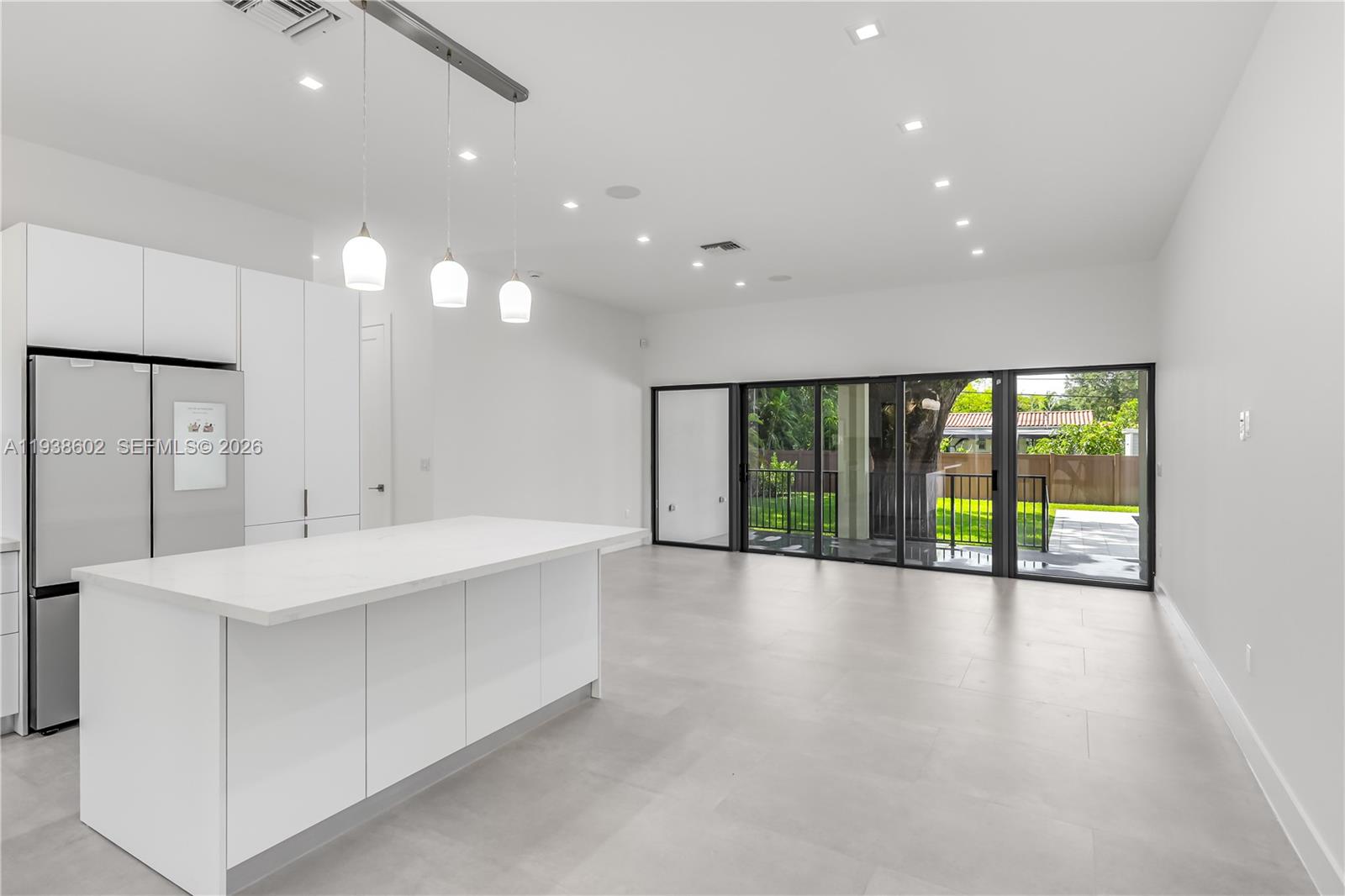 A modern kitchen with a white island and stainless refrigerator opens to a patio area — 1030 NE 121st St, Biscayne Park FL 33161, BISCAYNE PARK, FL