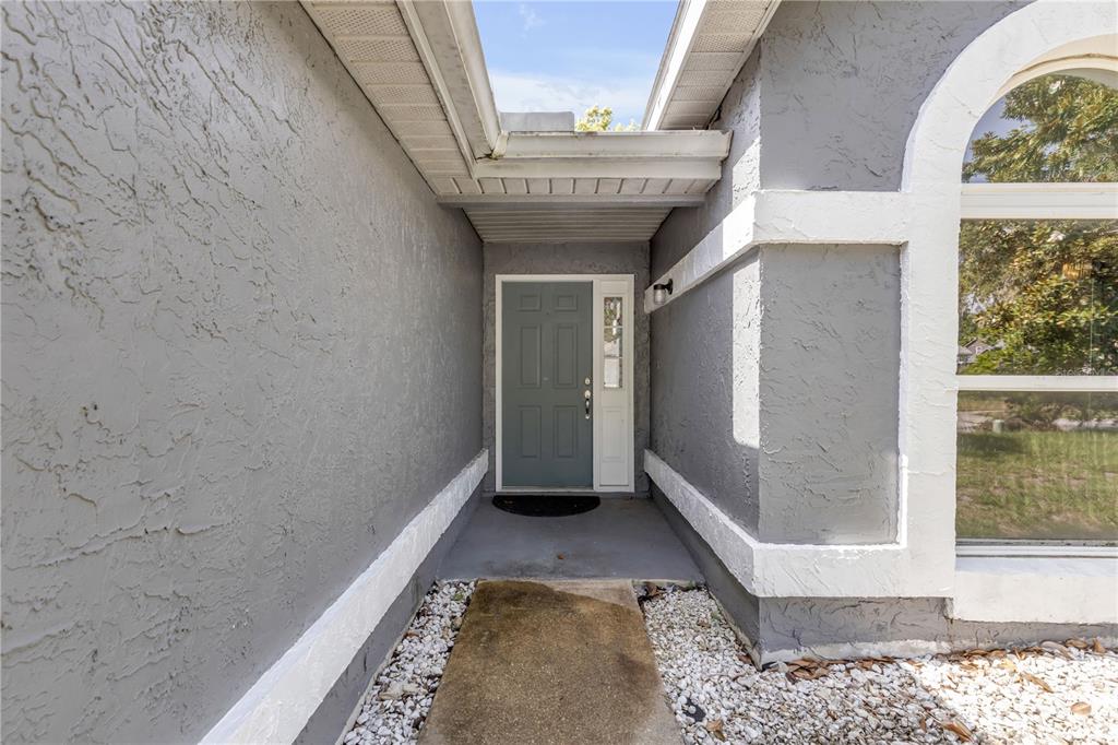 A gray front door with a sidelight is recessed within a stucco-walled entryway — 886 ANDKEN LANE, PORT ORANGE, FL