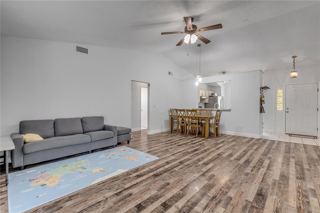 A living room with wood-look flooring, a gray sofa, and an adjacent dining area — 886 ANDKEN LANE, PORT ORANGE, FL
