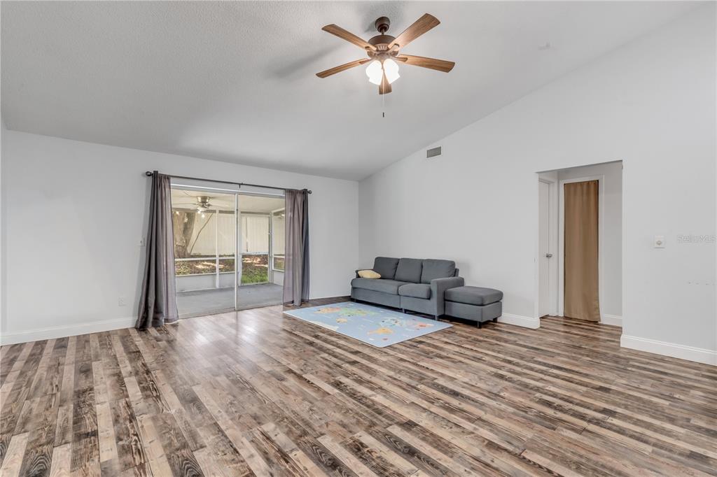 A living room with wood-look flooring, a ceiling fan, a sofa, and sliding glass doors — 886 ANDKEN LANE, PORT ORANGE, FL