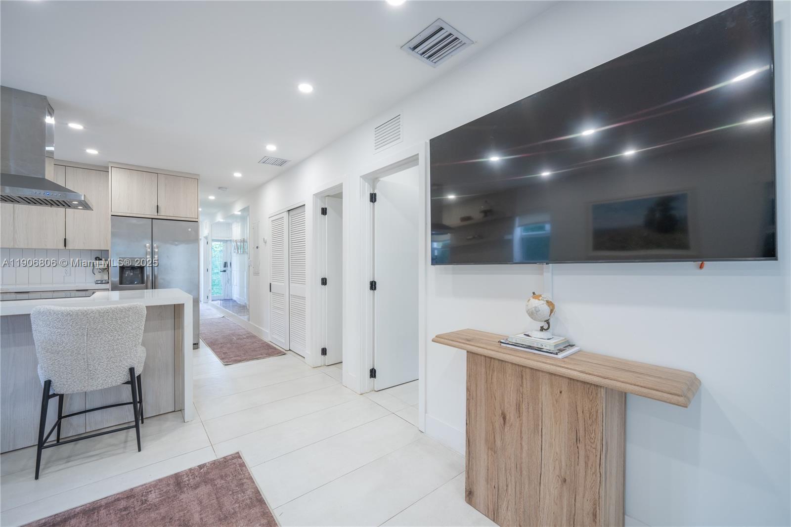 A modern kitchen and living area feature white tile floors, light wood cabinetry, and a television — 545 NW 47th St, Miami FL 33127, MIAMI, FL