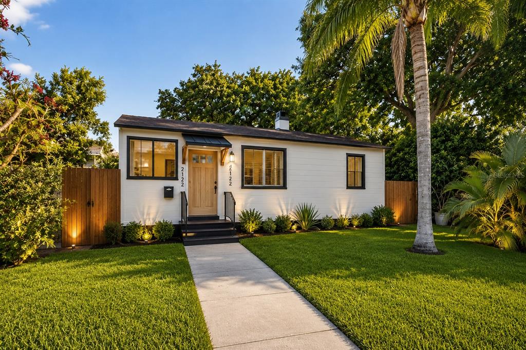 A single-story white house with black trim and a wooden door sits behind a lawn — 2122 6TH AVENUE N, ST PETERSBURG, FL