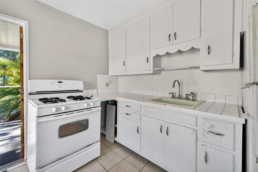 A kitchen with white cabinets, a white gas stove, and tiled countertops and flooring — 2122 6TH AVENUE N, ST PETERSBURG, FL