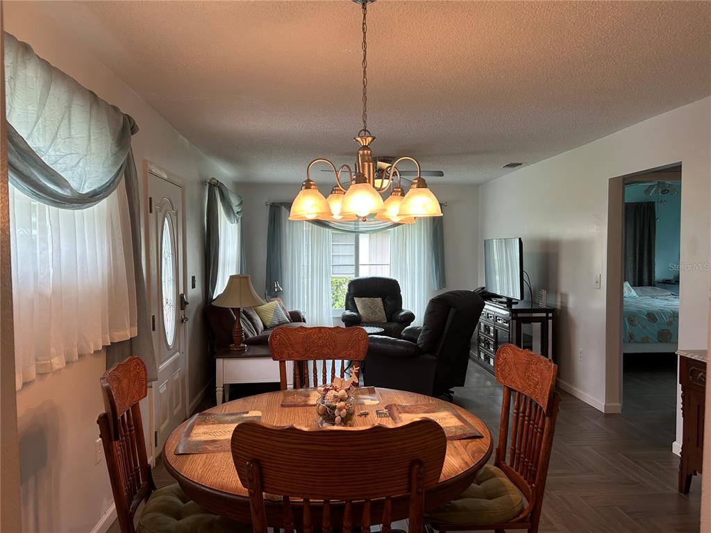 A dining area with a round wooden table and chairs sits before a living room — 1359 GLENDALE CIRCLE W UNIT 214, SARASOTA, FL