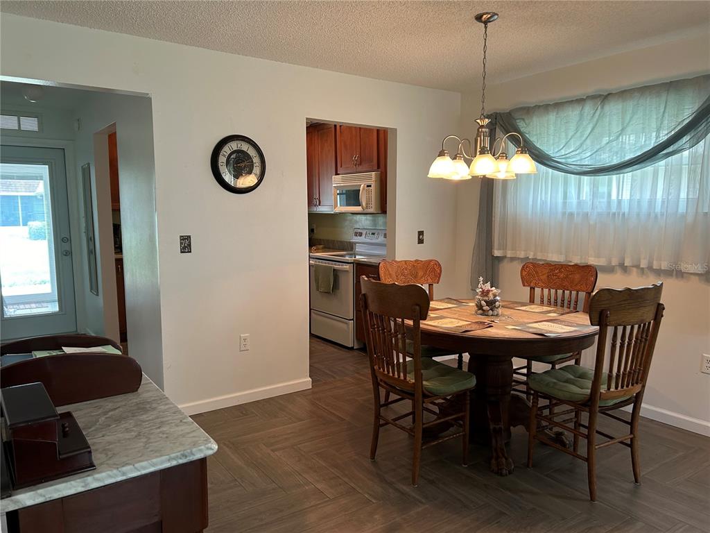 A dining area with a round wooden table and chairs sits adjacent to a kitchen — 1359 GLENDALE CIRCLE W UNIT 214, SARASOTA, FL