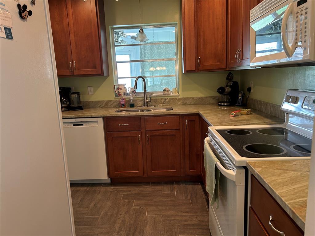 A kitchen features wood cabinets, stone countertops, a double sink, and a white electric range — 1359 GLENDALE CIRCLE W UNIT 214, SARASOTA, FL