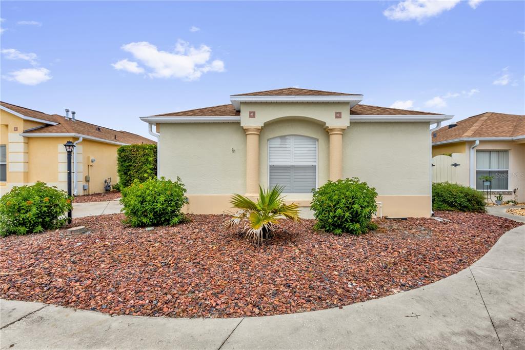 A single-story house with a beige stucco exterior, a brown shingled roof, and landscaped front yard — 1214 SAN BERNARDO ROAD, THE VILLAGES, FL