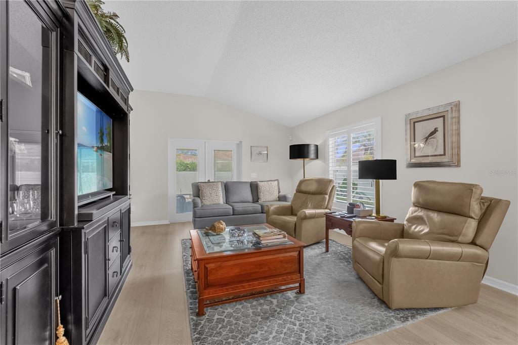 A living room features a black entertainment center, a gray sofa, two tan recliners, and wood-look flooring — 1214 SAN BERNARDO ROAD, THE VILLAGES, FL