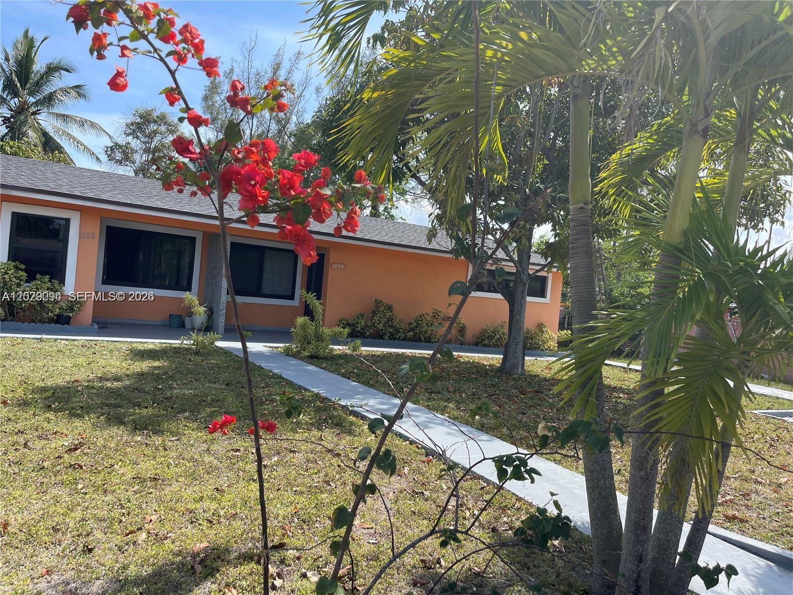 A single-story orange house features a walkway, palm trees, and a blooming bougainvillea in front — 1220 NE 116th St # 1222, Miami FL 33161, MIAMI, FL