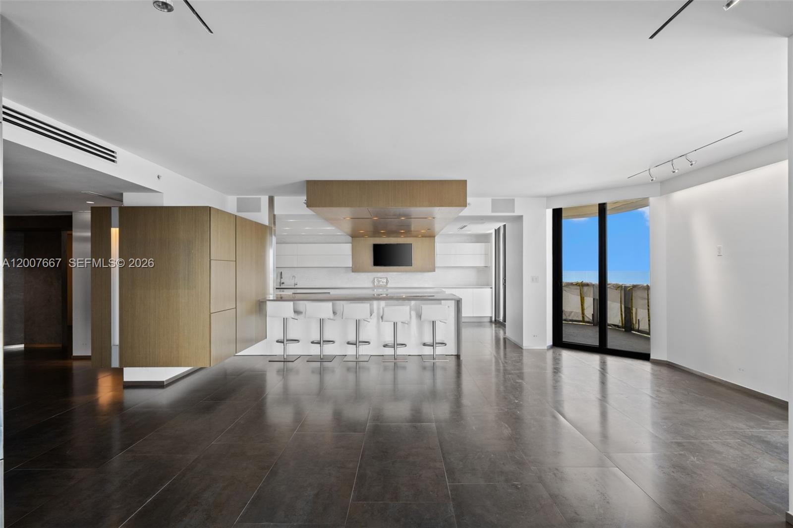 A modern kitchen with a wood-paneled island, white cabinetry, and dark tile flooring — 9999 Collins Ave # 6J, Bal Harbour FL 33154, BAL HARBOUR, FL