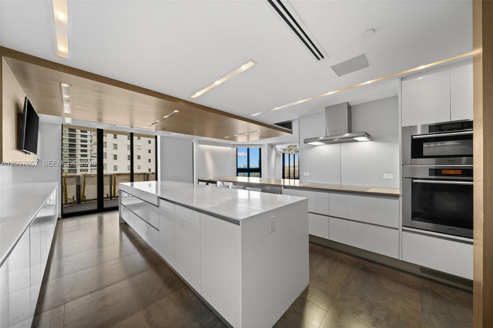 A modern kitchen features a large white island, sleek cabinetry, and a wood-paneled ceiling — 9999 Collins Ave # 6J, Bal Harbour FL 33154, BAL HARBOUR, FL