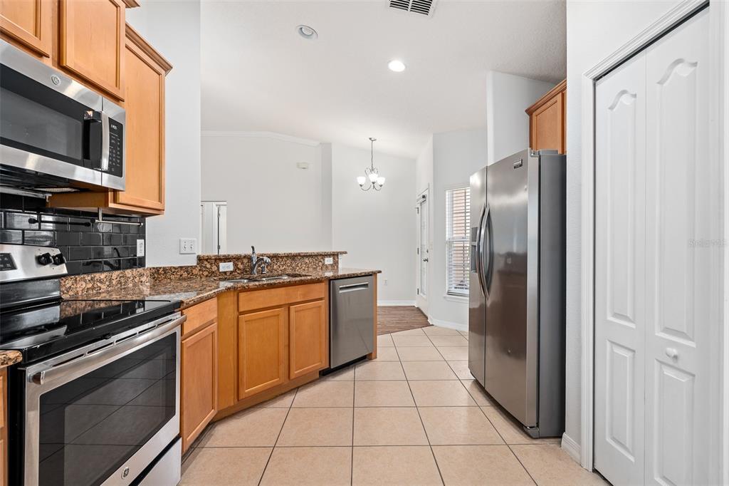 A kitchen features wood cabinets, granite countertops, stainless steel appliances, and beige tile flooring — 5317 PEACH BLOSSOM BOULEVARD, PORT ORANGE, FL