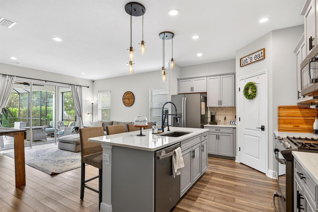 A modern kitchen with a gray island, white countertops, and stainless steel appliances overlooks a living area — 13852 OLD CREEK COURT, PARRISH, FL
