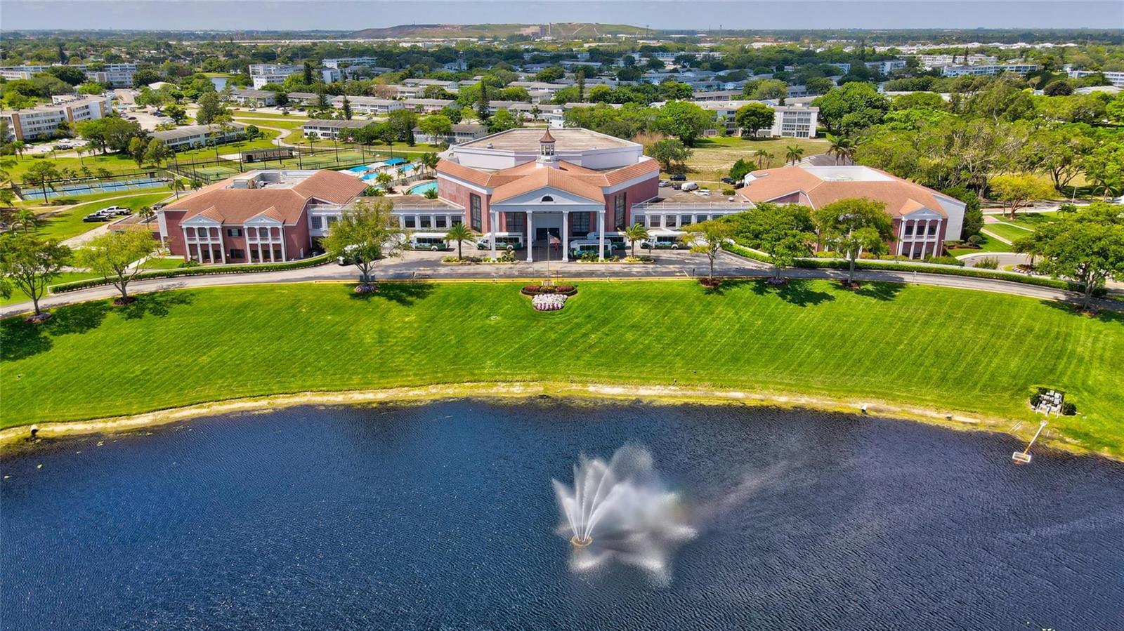 An aerial view shows a large building with a fountain in a foreground lake — 284 Grantham F, Deerfield Beach FL 33442, DEERFIELD BEACH, FL