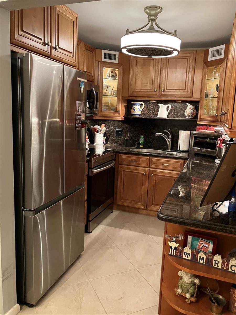 A kitchen features wood cabinets, stainless steel appliances, dark granite countertops, and tile flooring — 284 Grantham F, Deerfield Beach FL 33442, DEERFIELD BEACH, FL