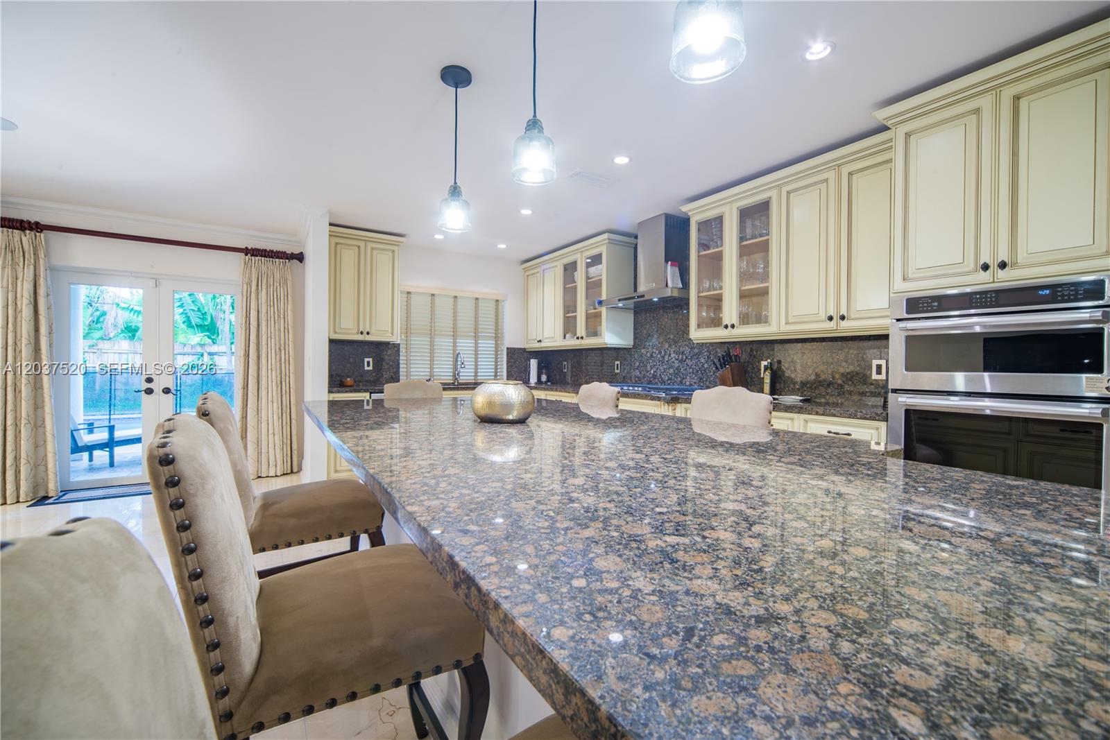 A kitchen features a large granite island, cream-colored cabinetry, stainless steel appliances, and glass doors — 3514 Crystal Ct, Miami FL 33133, MIAMI, FL
